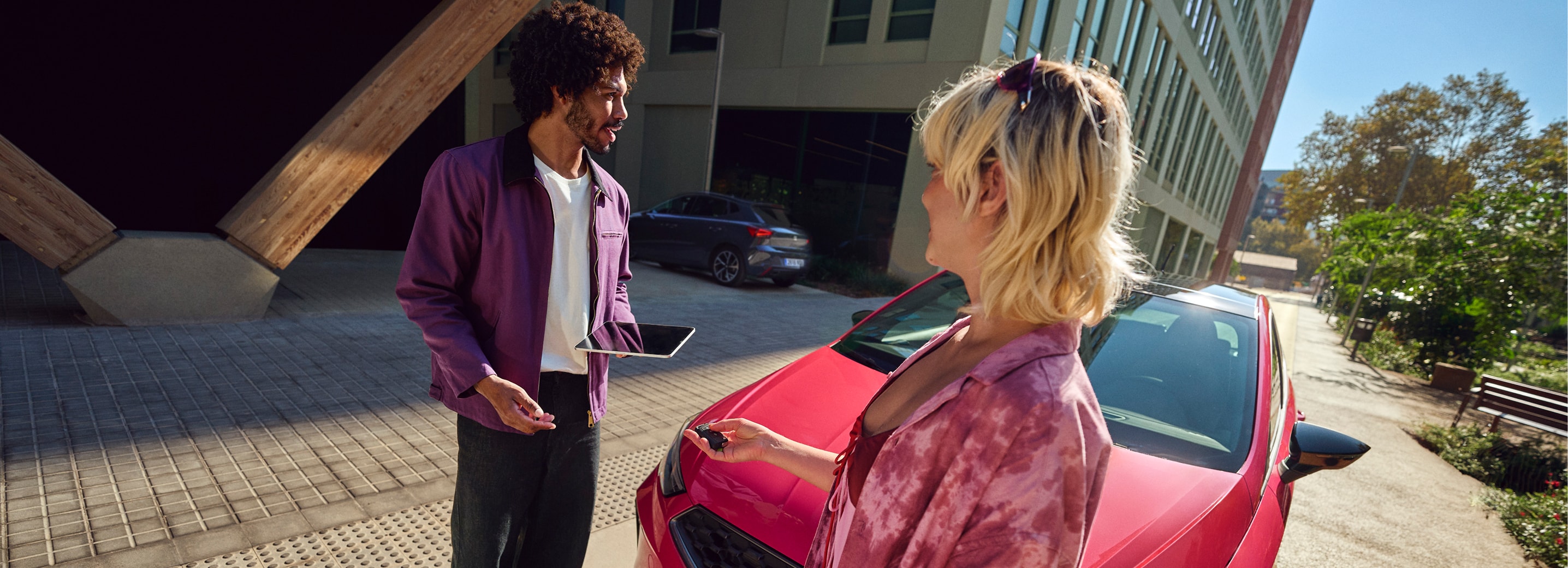 Two people standing next to a red SEAT Ibiza in an urban setting, holding car keys and a tablet