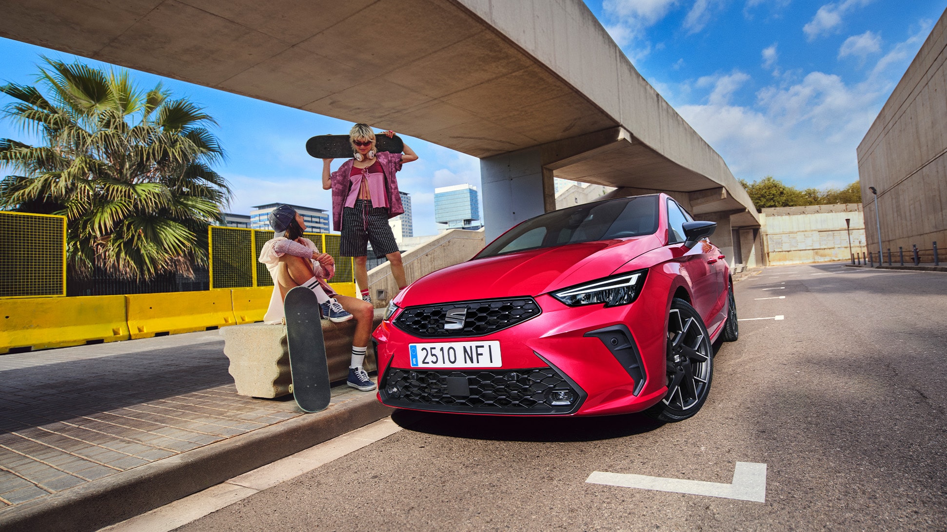 SEAT Ibiza in vibrant red parked on an urban street under a modern bridge with two people and a skateboard