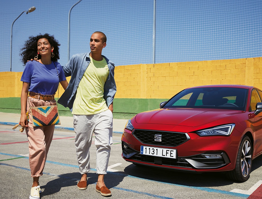 two women talking and laughing to each other in the street next to a SEAT Arona in desire red color